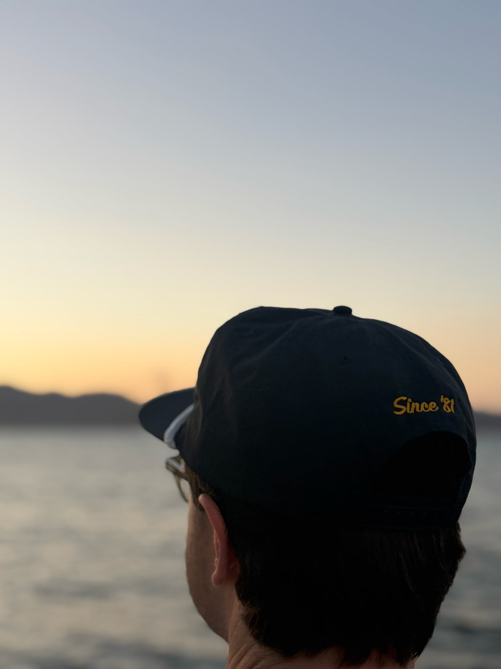 Back view of the navy Fleet Week hat worn by the waterfront at sunset